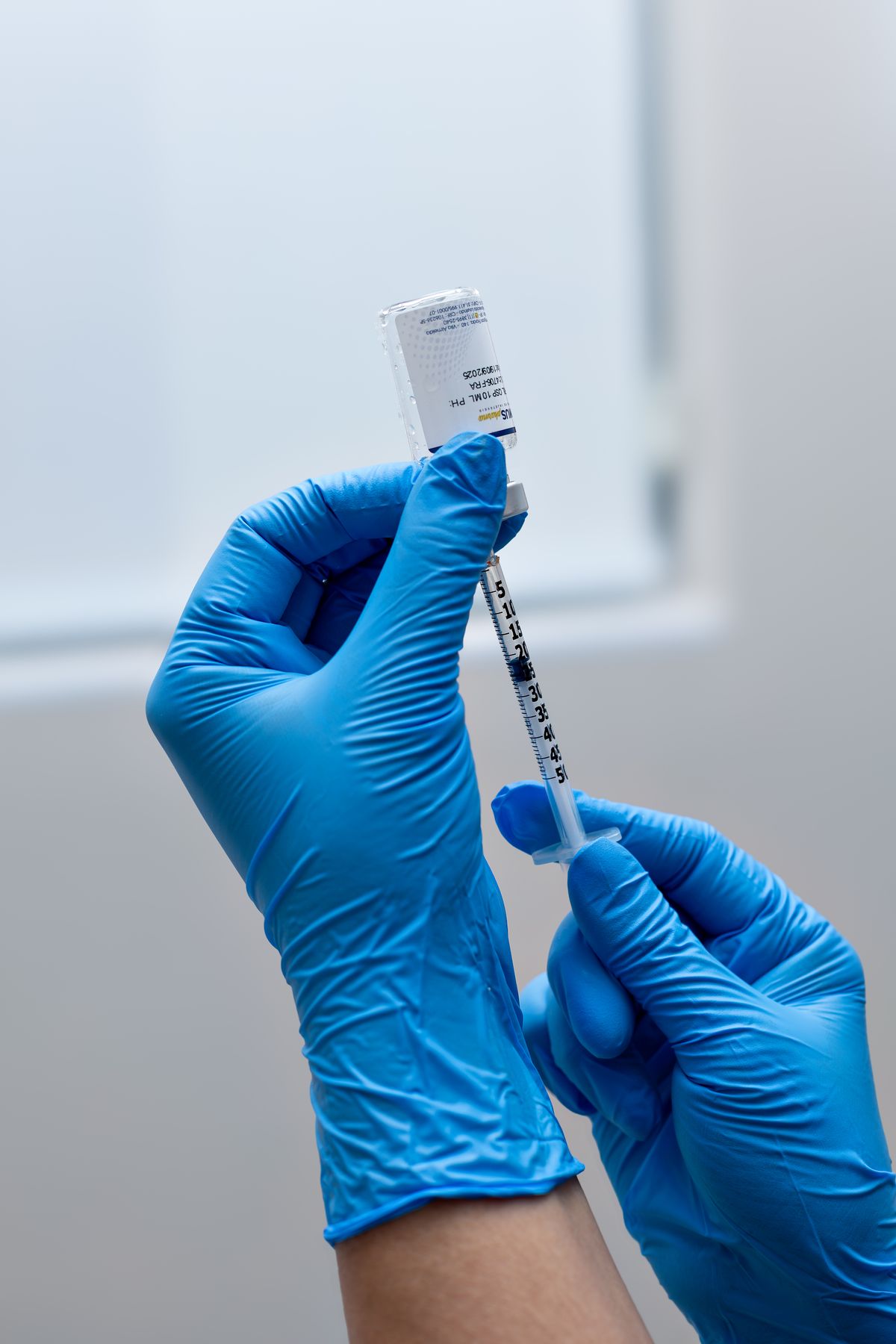 A gloved hand preparing a syringe from a vial