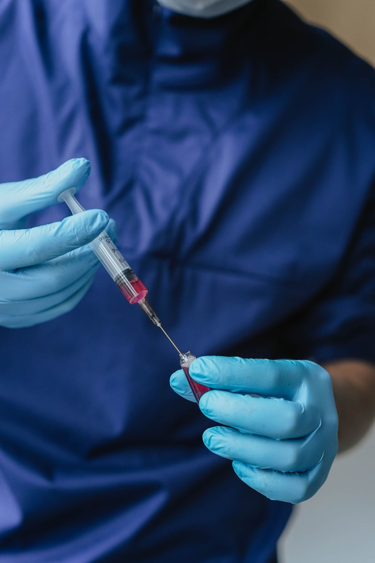 A gloved hand drawing medicine into a syringe