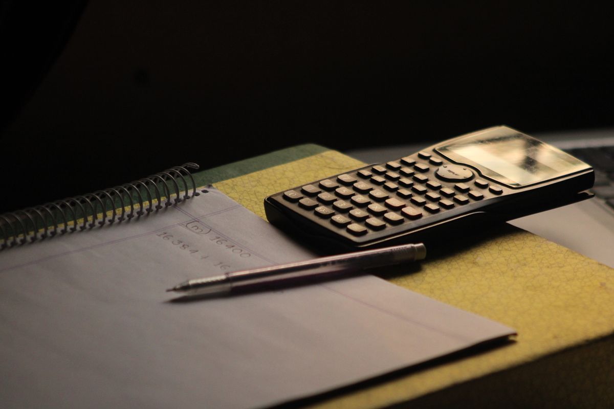 A scientific calculator, a pen and a ruled notebook on a desk
