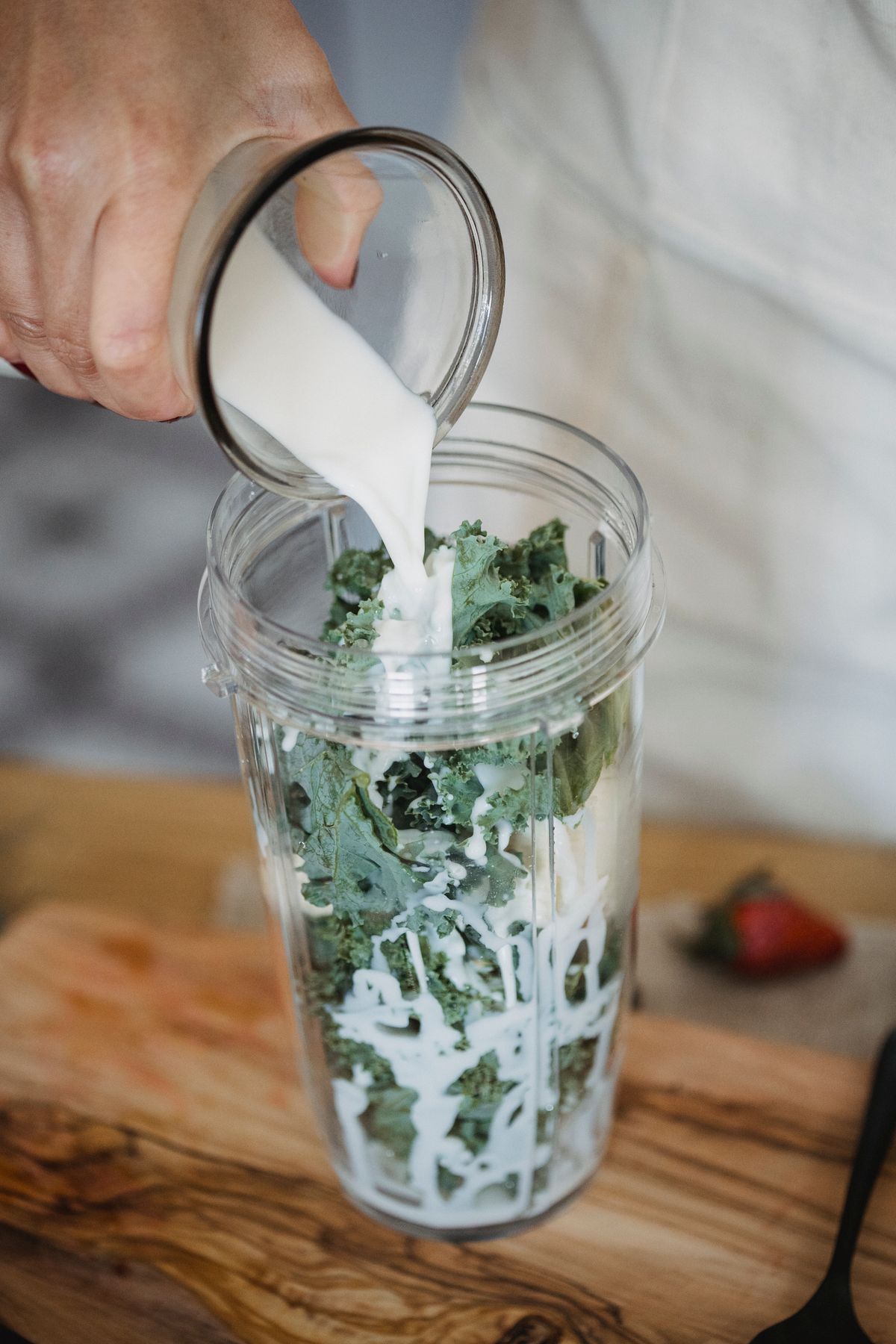 Milk being poured over leafy green vegetables in a jar