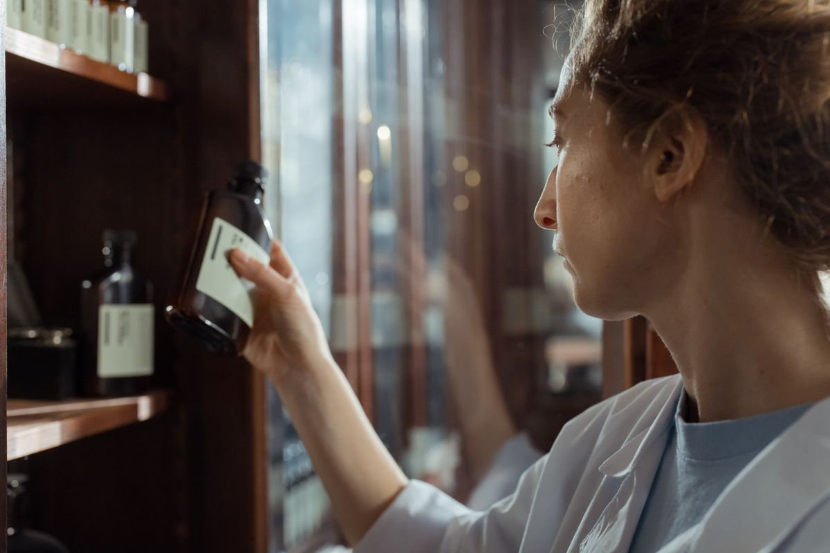 A pharmacist in a white coat reading the label on a medicine bottle from a shelf