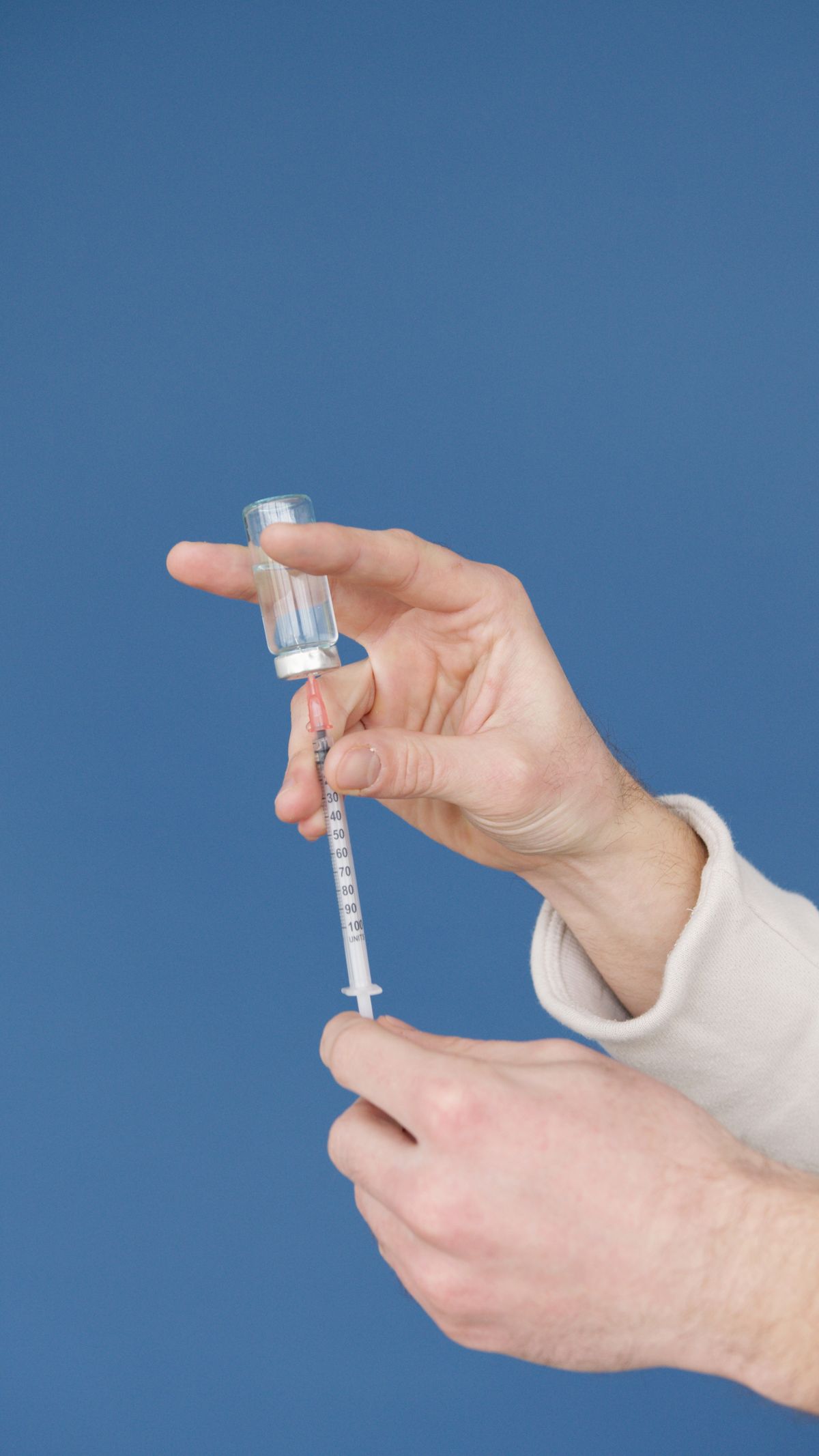 Hands holding a small vial and a syringe against a blue background