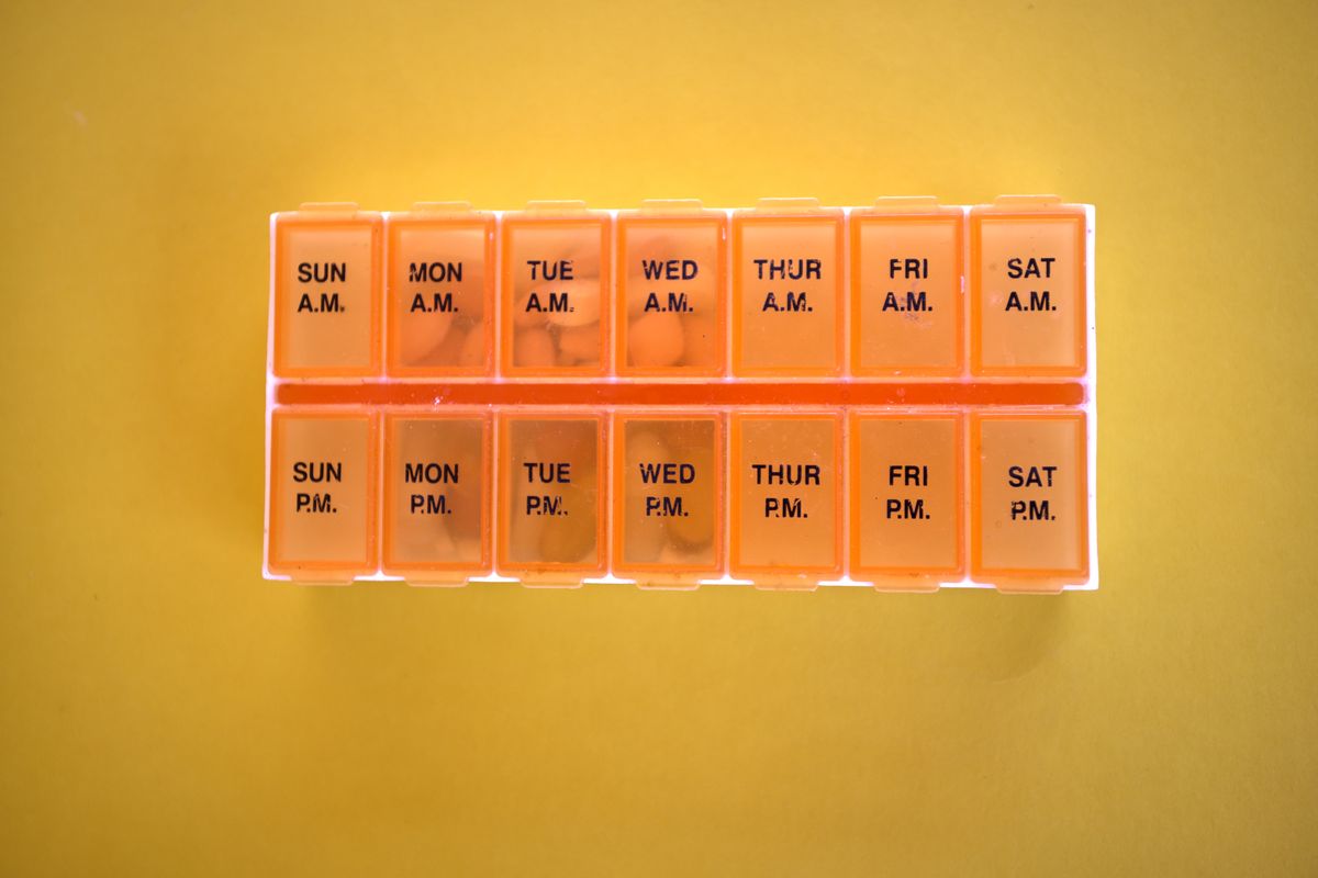 A weekly pill organiser on a yellow background
